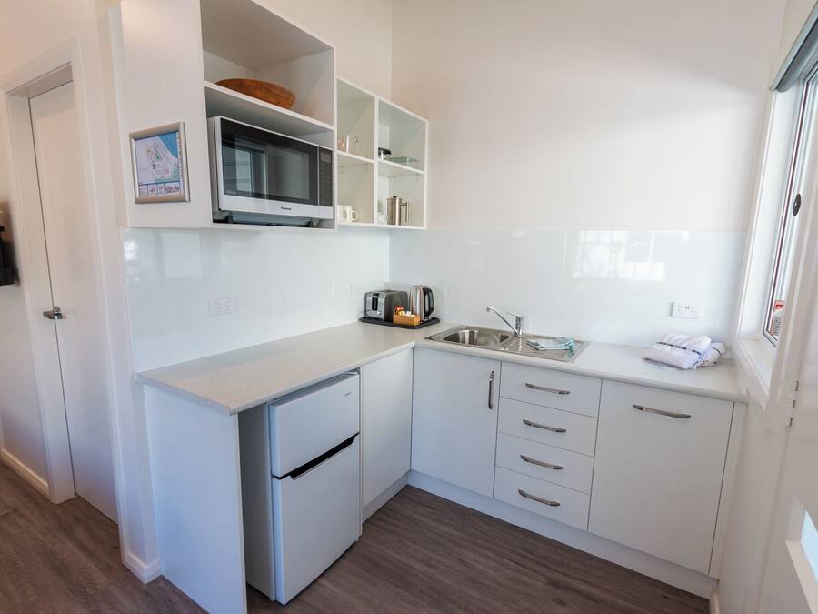 Een kleine keuken met witte kasten, een magnetron, een broodrooster en een spoelbak.