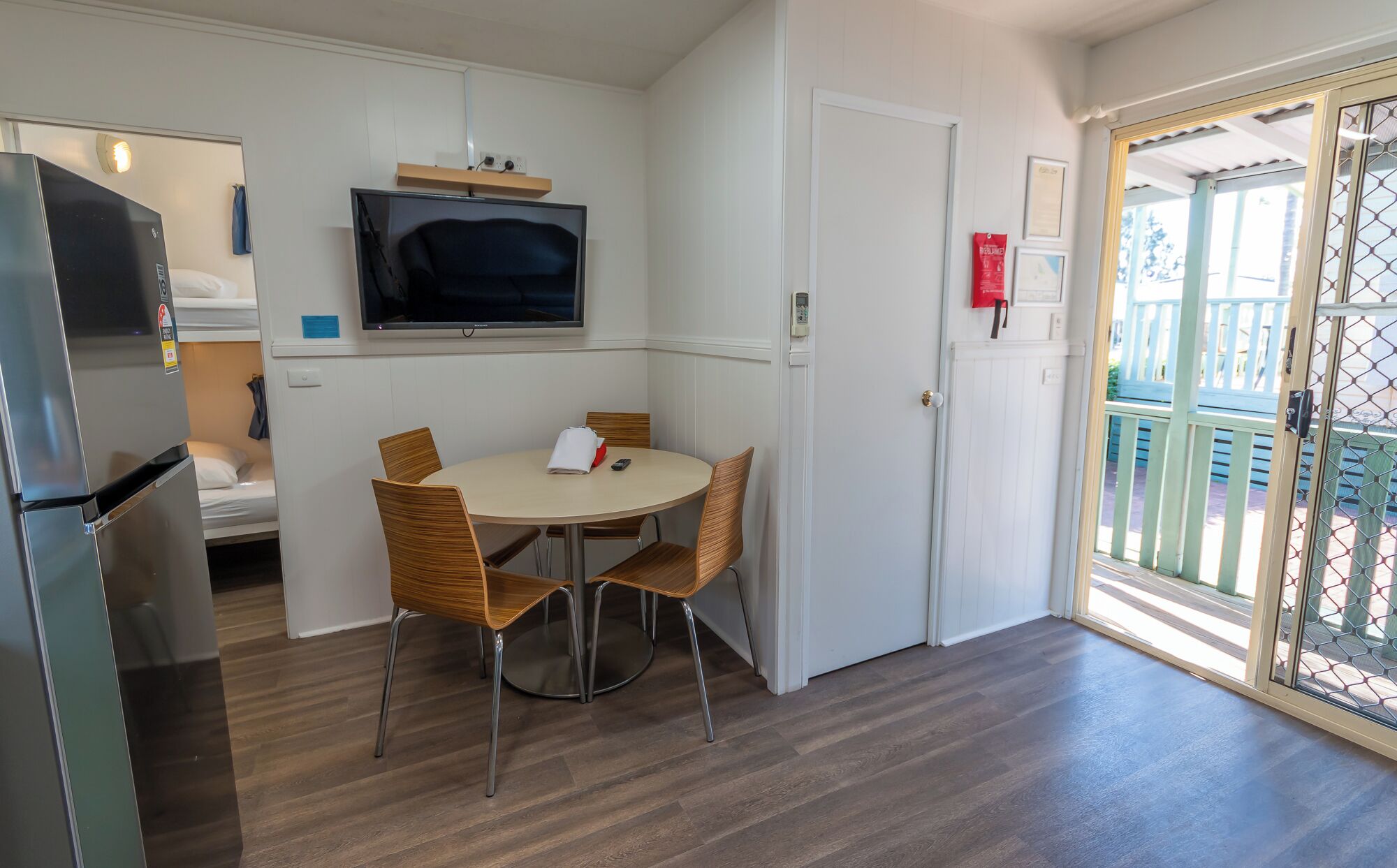A compact kitchen with a dining table, chairs, a TV, and a refrigerator.