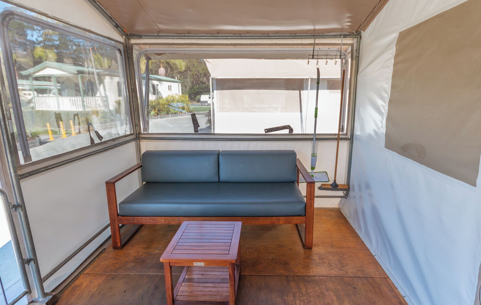 Um quarto com tenda, um banco de madeira, um sofá azul e uma janela com vista para uma casa e árvores.