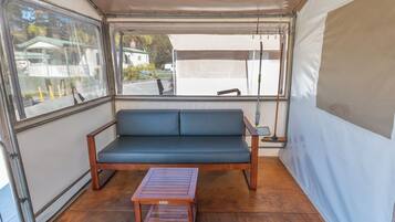Um quarto com tenda, um banco de madeira, um sofá azul e uma janela com vista para uma casa e árvores.