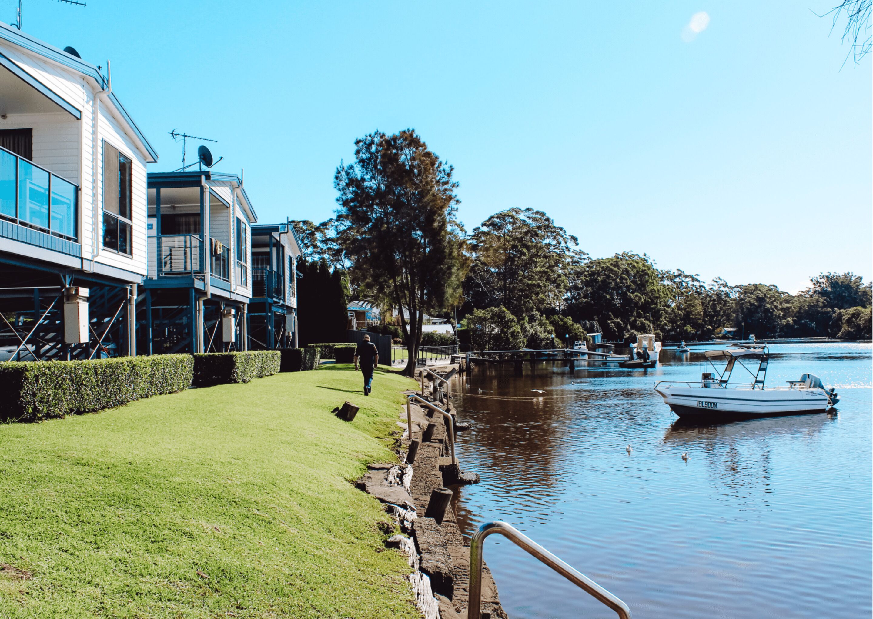 A riverside property with a grassy lawn, a wooden dock, and a boat.