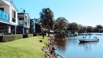 A riverside property with a grassy lawn, a wooden dock, and a boat.
