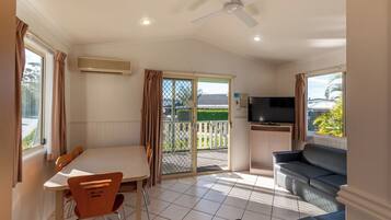 A room with a dining table and chairs, a sofa, a TV, and a ceiling fan.