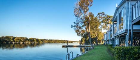 A lakeside property with a dock, a grassy area, and a building with a balcony.