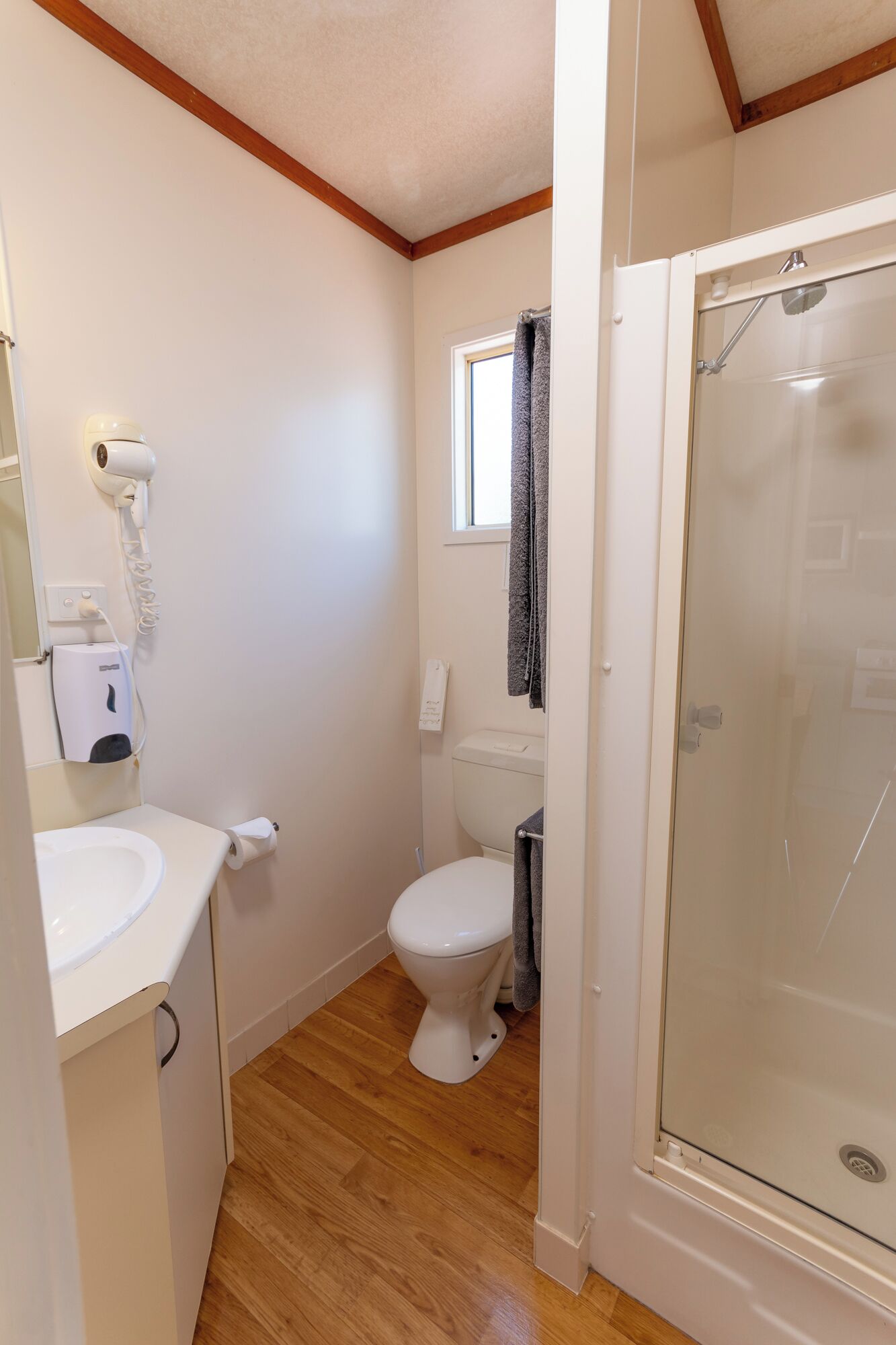 A compact bathroom with a toilet, a hand dryer, and a glass shower enclosure.