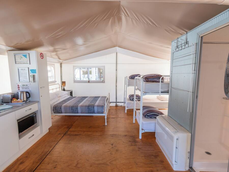 A compact, well-lit tent with a kitchenette, a single bed, and a bunk bed.
