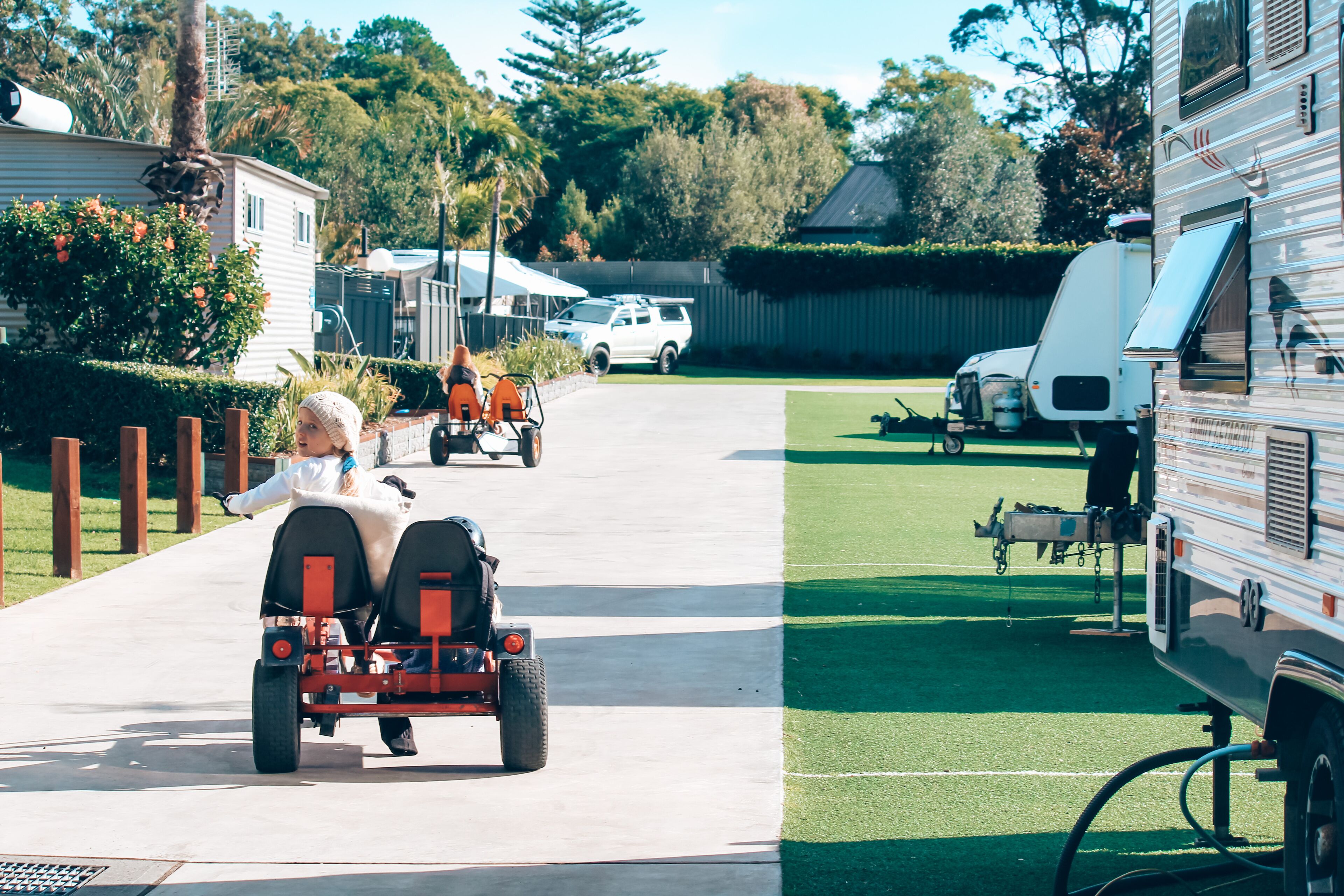 Uma rua residencial com um parque de trailers ao fundo.
