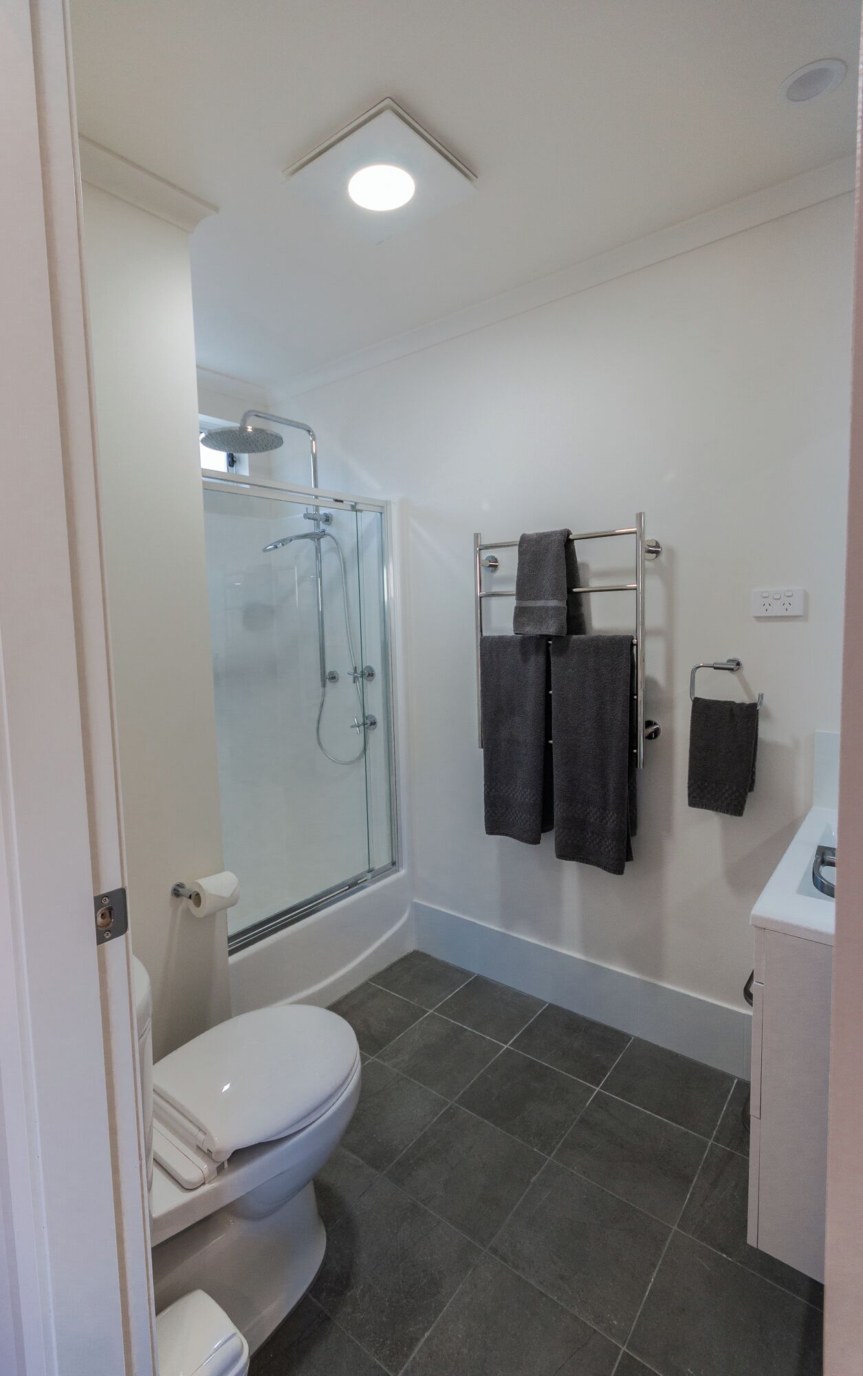 A modern bathroom with a glass-enclosed shower, a white toilet, and a towel rack with multiple towels.