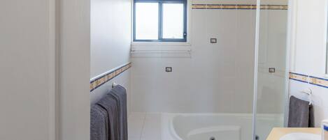 A bathroom with a bathtub, a shower, a sink, and a window.
