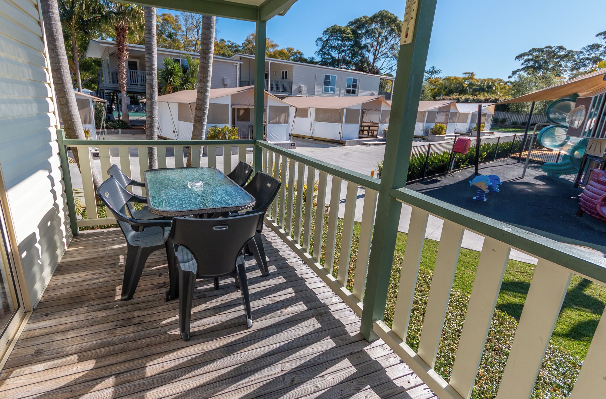 A wooden deck with a table and chairs, a fenced area, and a playground with a slide and swings.