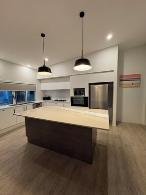 Una cocina moderna con una isla central, electrodomésticos de acero inoxidable e iluminación colgante.