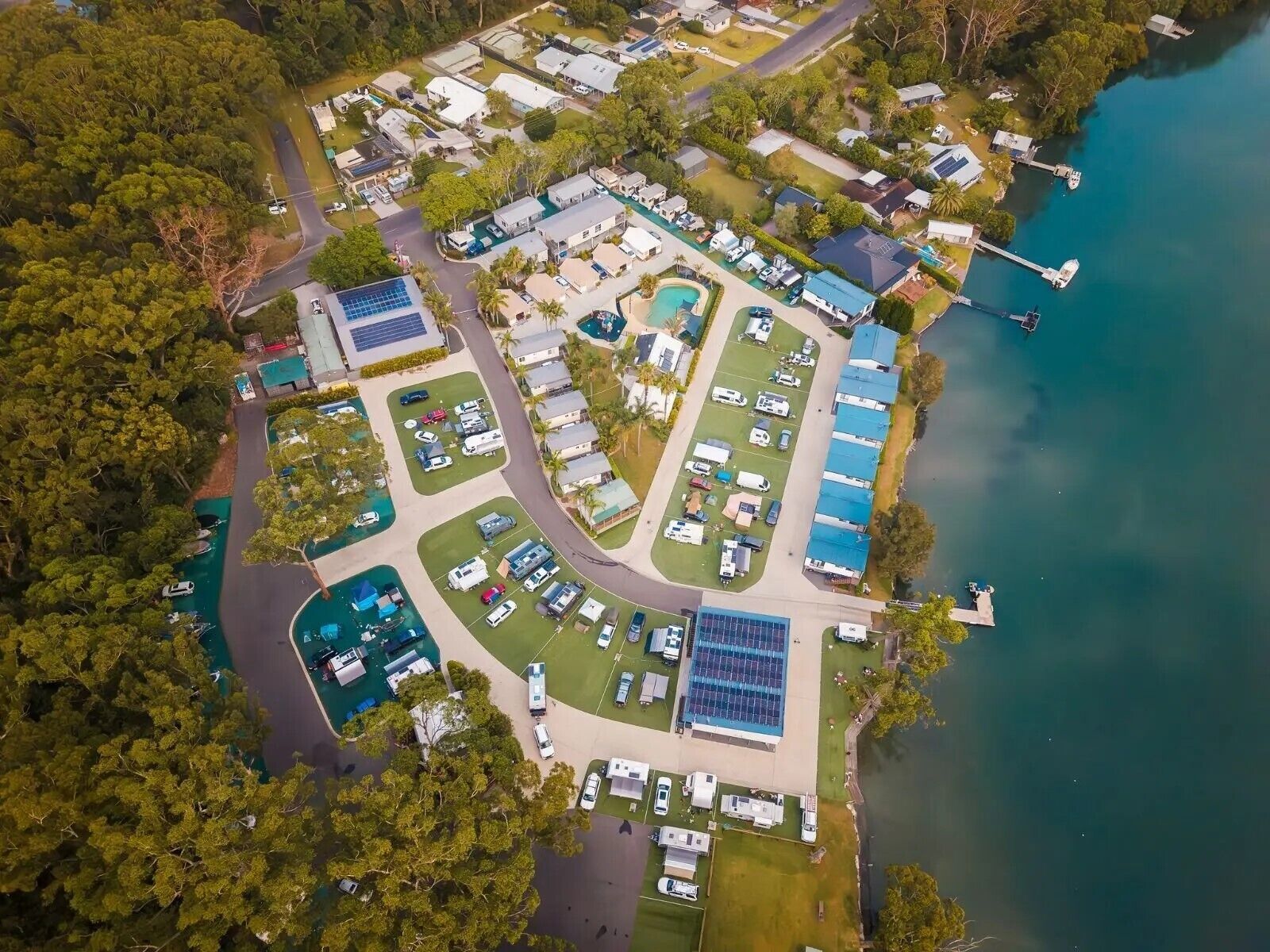 Eine Luftaufnahme eines Campingplatzes mit Wohnmobilen, Solaranlagen und einem See.
