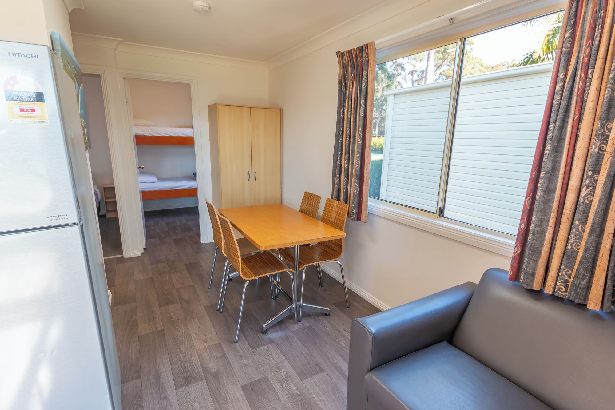 A compact room with a bunk bed, a dining table with chairs, a refrigerator, and a sofa.