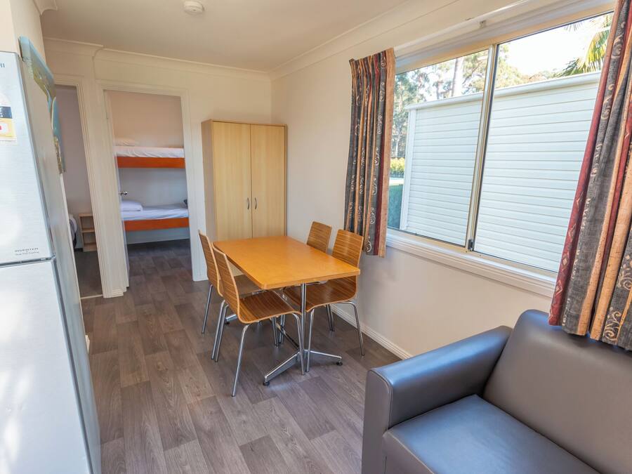 A compact room with a bunk bed, a dining table with chairs, a refrigerator, and a sofa.