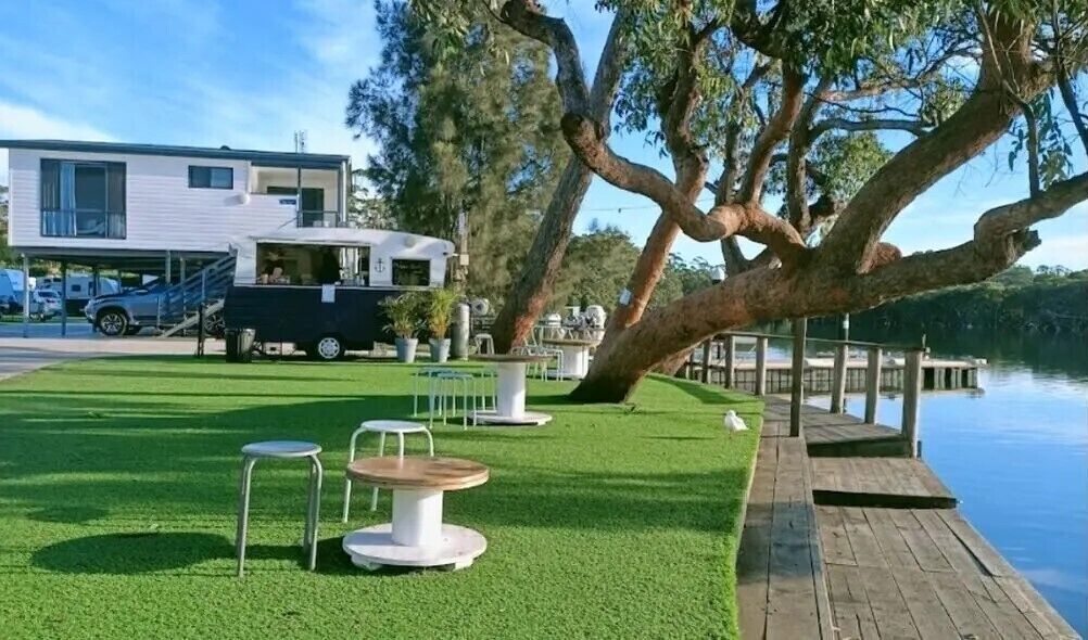 A lakeside outdoor area with a dining table and chairs, a covered seating area, and a dock extending into the water.