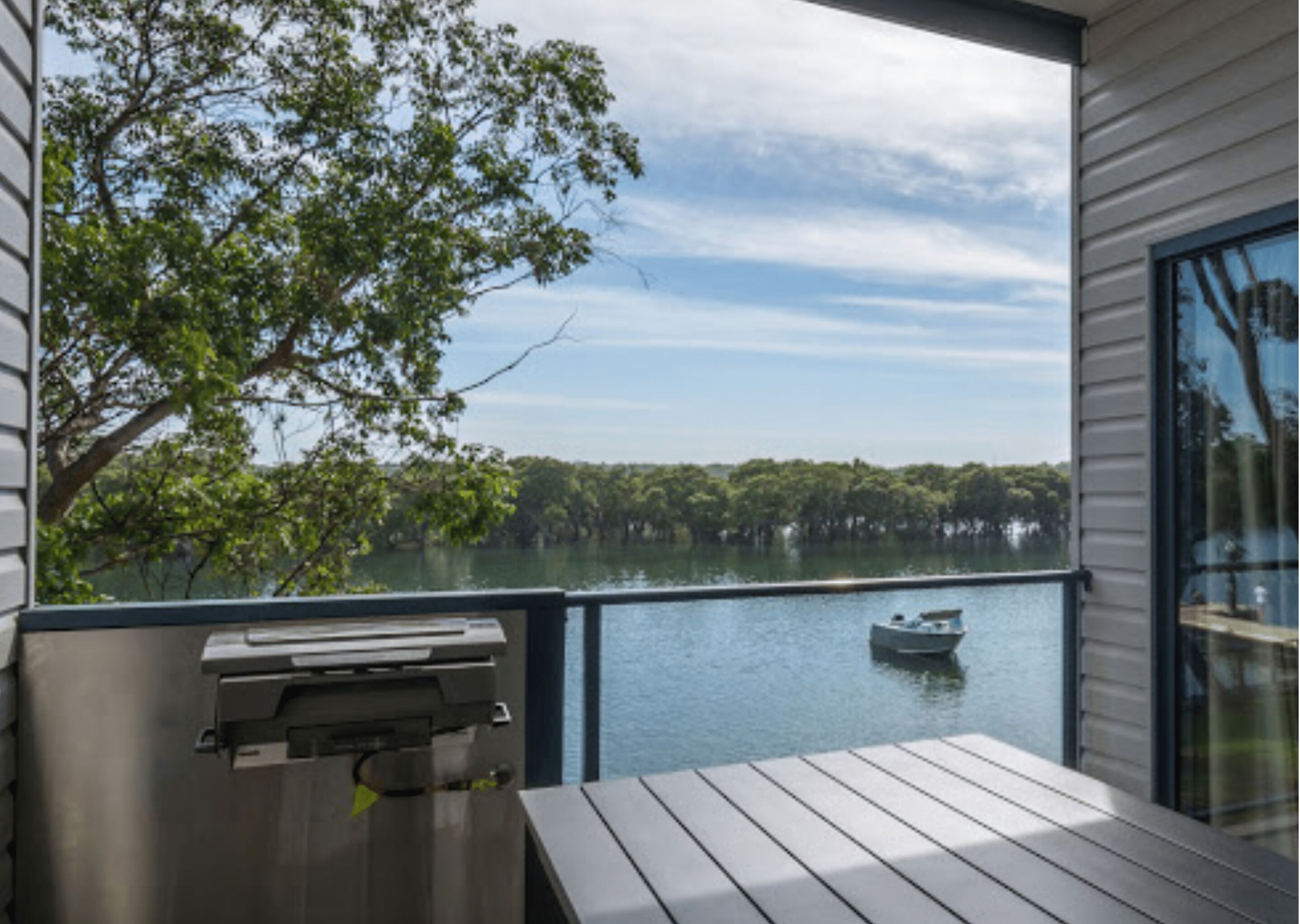A balcony with a view of a lake, a boat, and a grill.