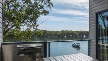 A balcony with a view of a lake, a boat, and a grill.