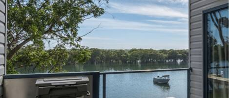 A balcony with a view of a lake, a boat, and a grill.