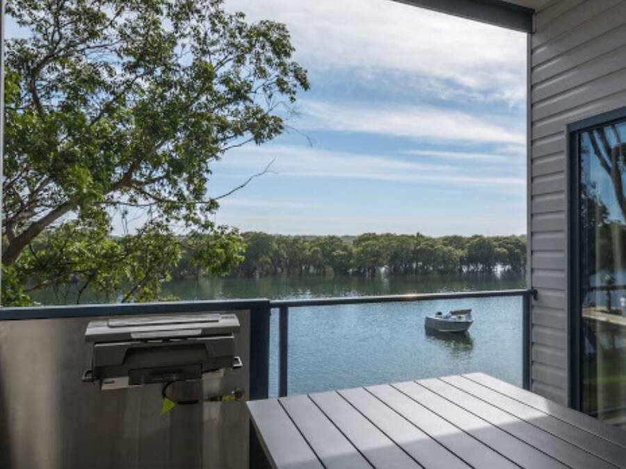 A balcony with a view of a lake, a boat, and a grill.