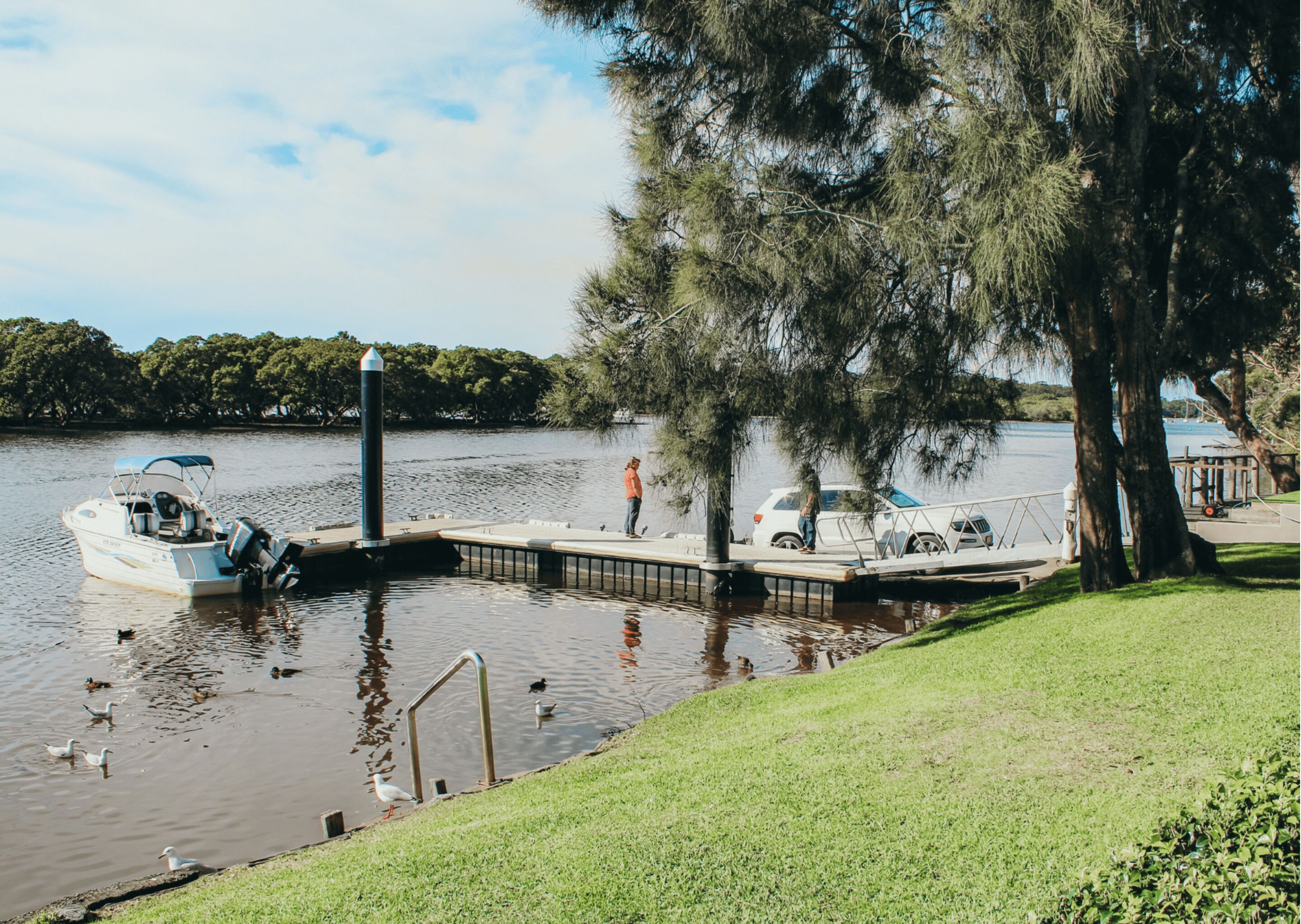 A dock with a boat, a person standing by the dock, and a grassy area with trees.