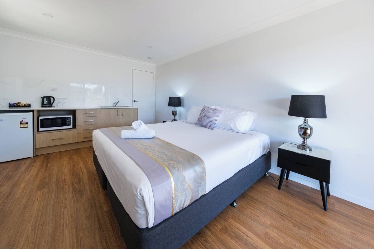 A hotel room with a bed, bedside tables, a desk with a microwave, and a small kitchenette.