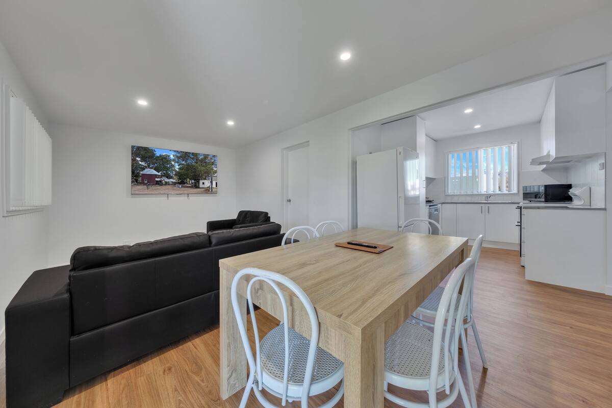 A modern living space with a dining area, a black sofa, white chairs, and a wooden table.
