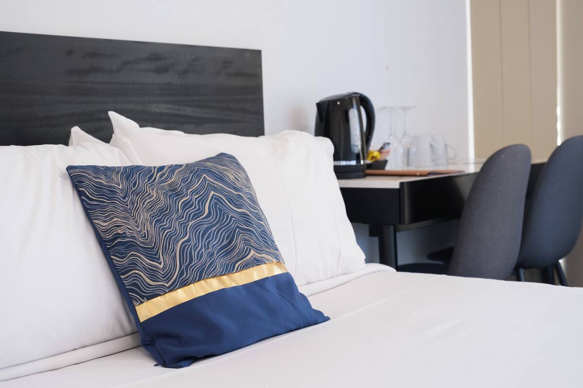 A hotel room with a bed, a desk with a coffee maker, and a chair.