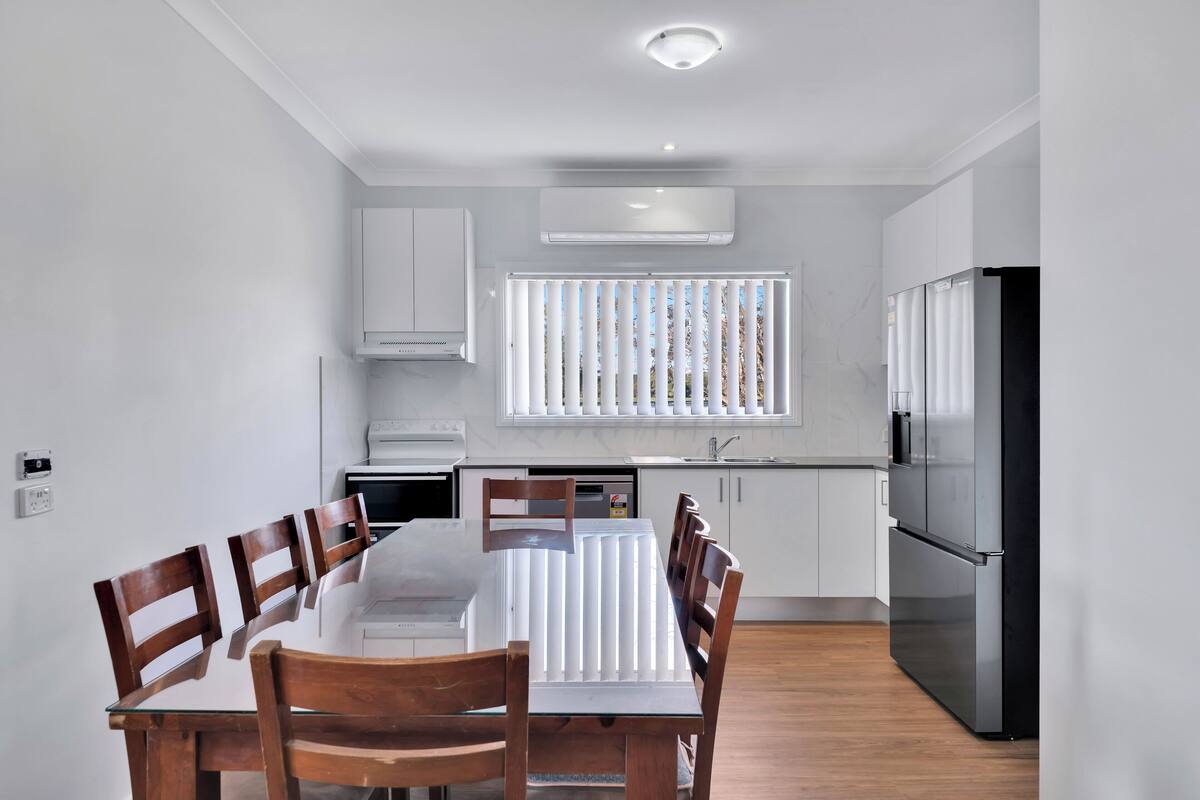 A modern kitchen with white cabinets, a black refrigerator, and a dining table with wooden chairs.