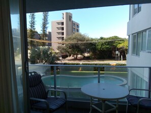 A balcony with a pool, two striped chairs, and a table. - Amira Apartments (Main Beach)