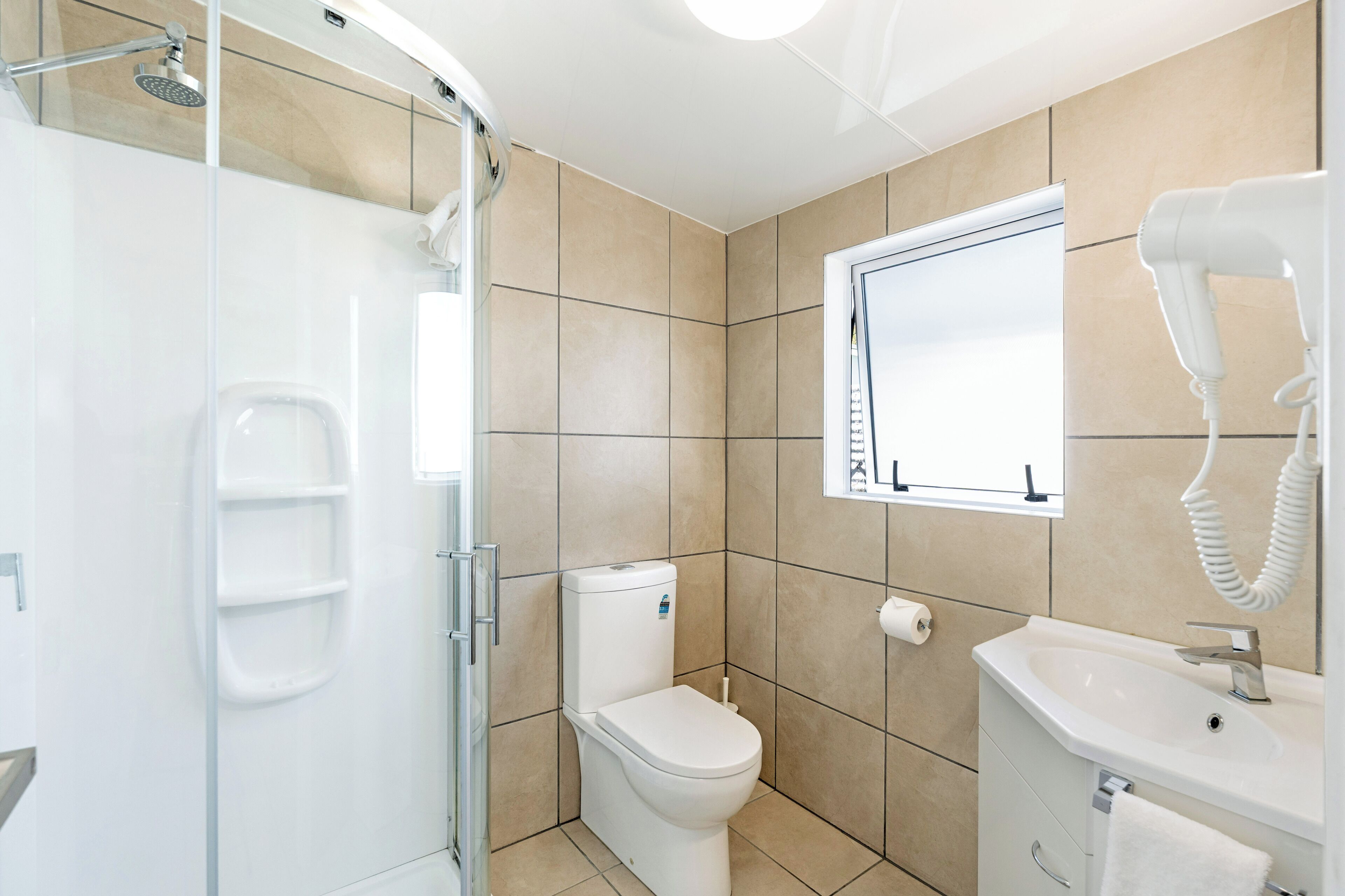 Un baño moderno con cabina de ducha de vidrio, inodoro, lavamanos y secador de pelo.