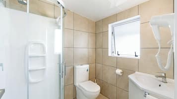 Un baño moderno con cabina de ducha de vidrio, inodoro, lavamanos y secador de pelo.