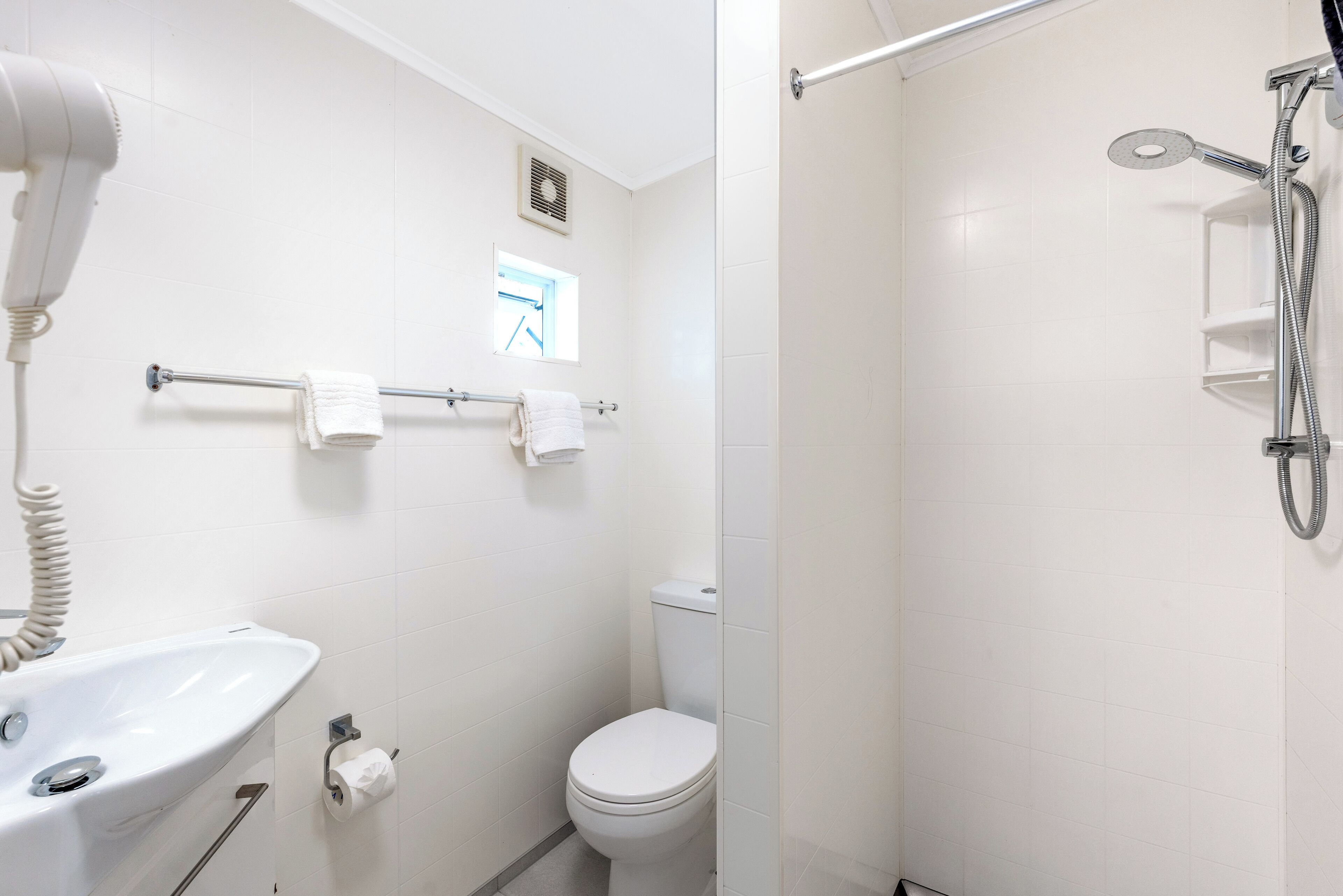 A bathroom with a sink, toilet, towel rack, and a shower area.
