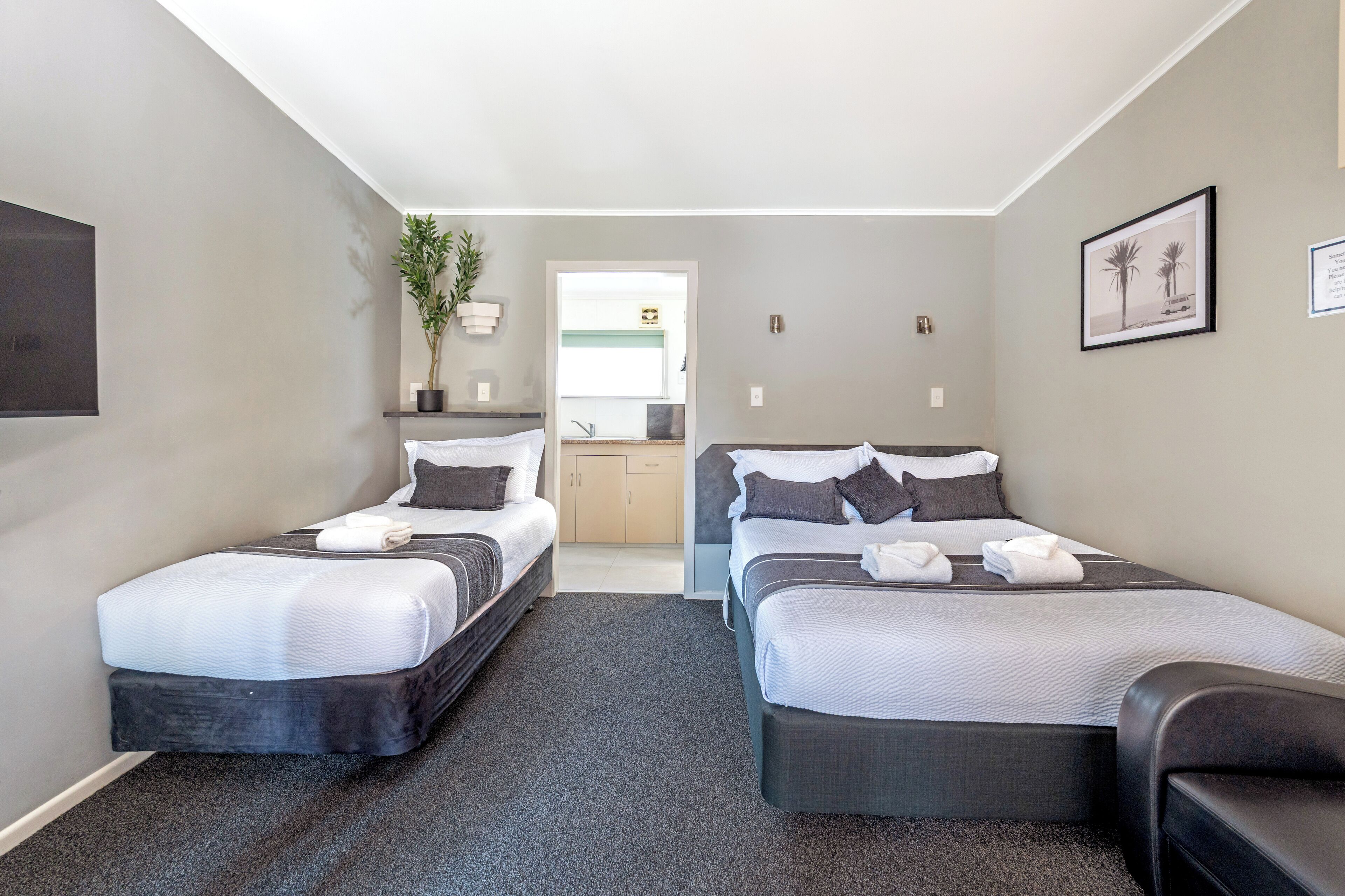 A hotel room with two beds, a small seating area, a potted plant, and a view into the kitchen area.