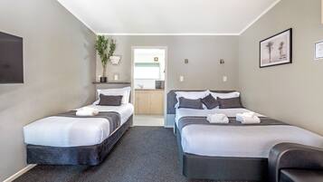 A hotel room with two beds, a small seating area, a potted plant, and a view into the kitchen area.