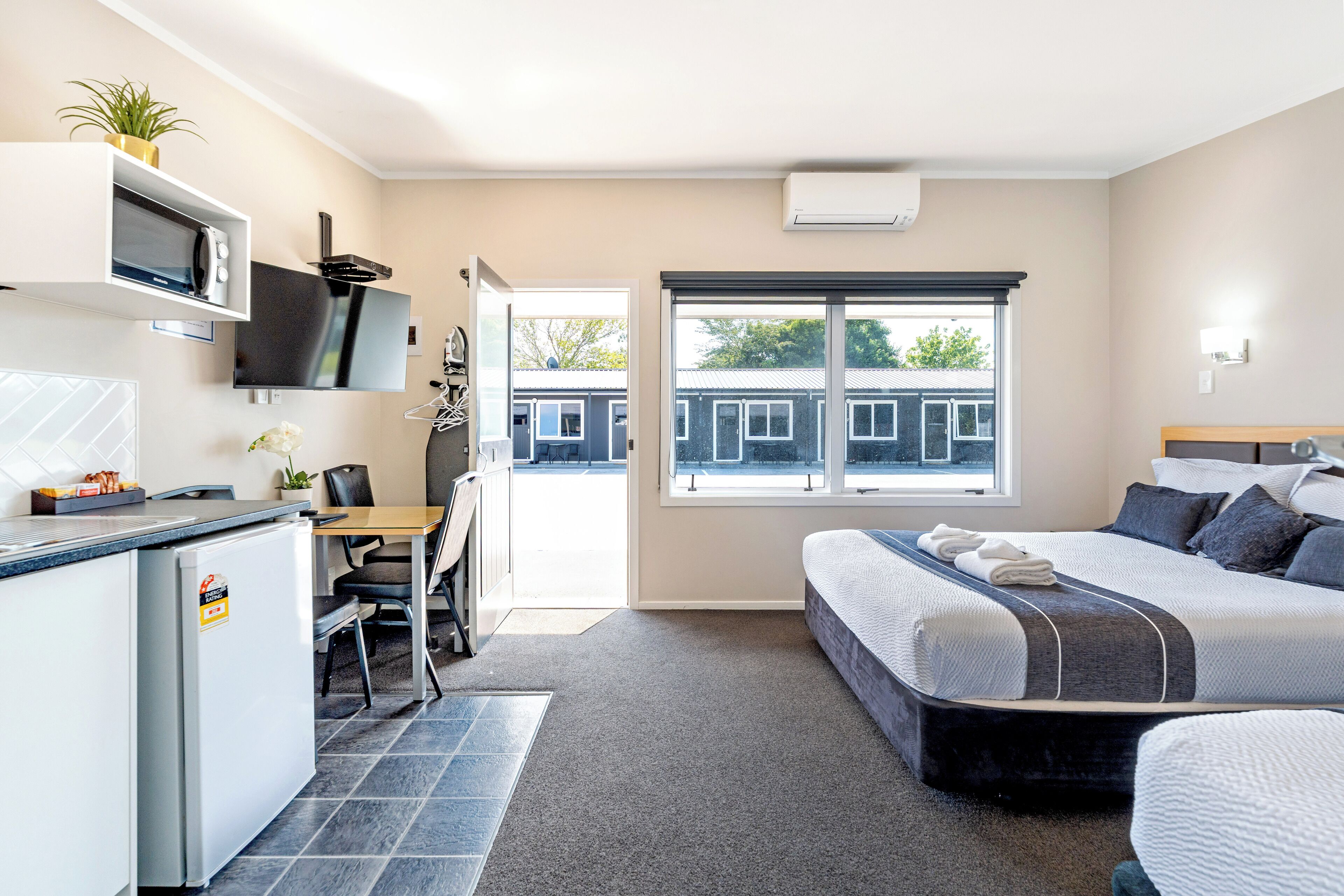 Habitació d'hotel moderna amb llit, escriptori, petita cuina i finestra gran.