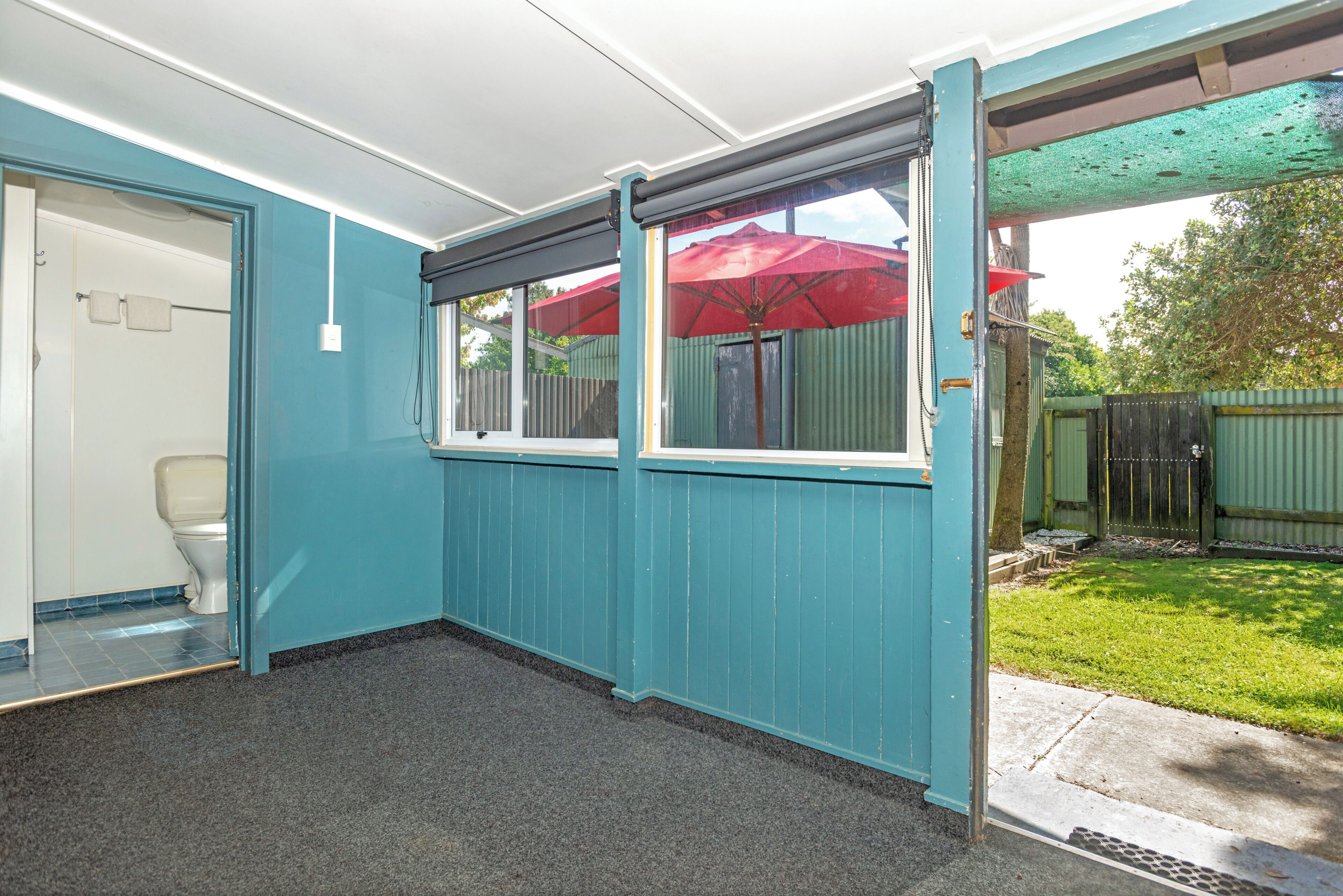 A bathroom with a toilet, a shower, and a window with a red umbrella outside.