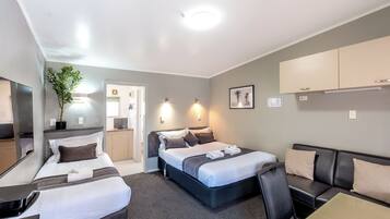 A hotel room with two beds, a sofa, a desk, a mirror, and a potted plant.