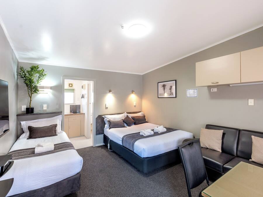 A hotel room with two beds, a sofa, a desk, a mirror, and a potted plant.