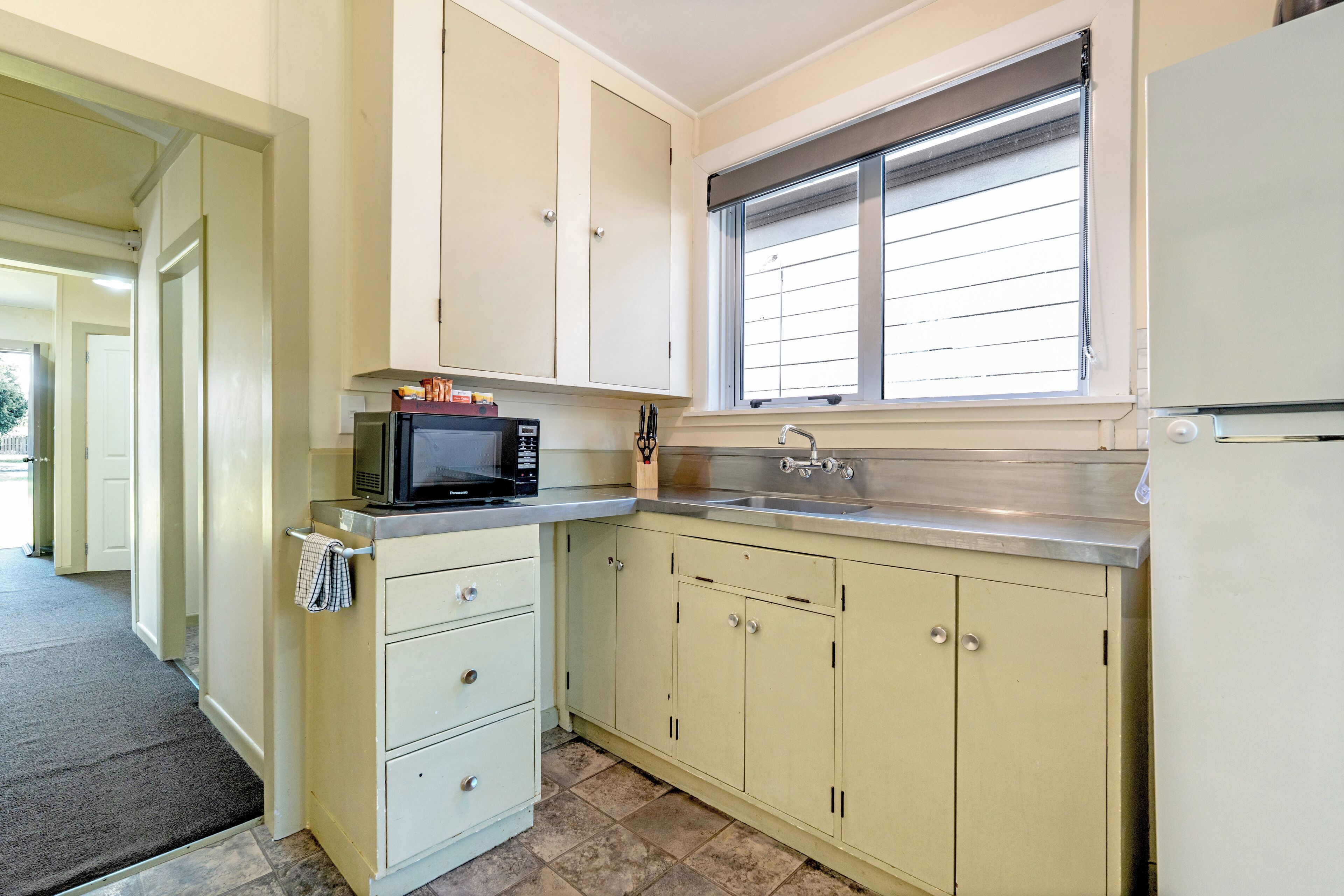 A kitchen with cabinets, a microwave, a sink, and a window with blinds.