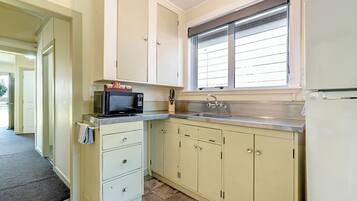 A kitchen with cabinets, a microwave, a sink, and a window with blinds.