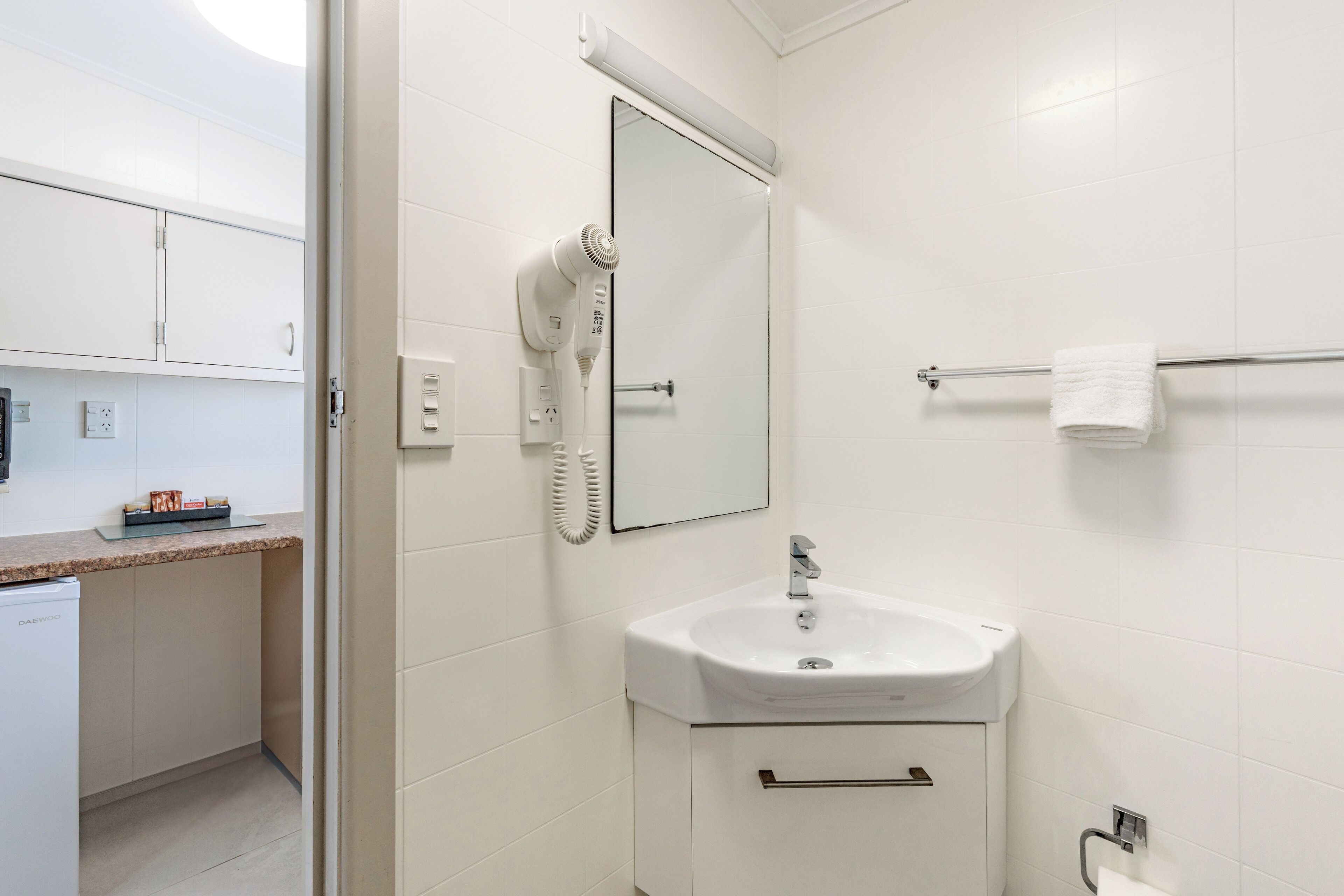 A bathroom with a white sink, a mirror, a towel rack, and a hairdryer.