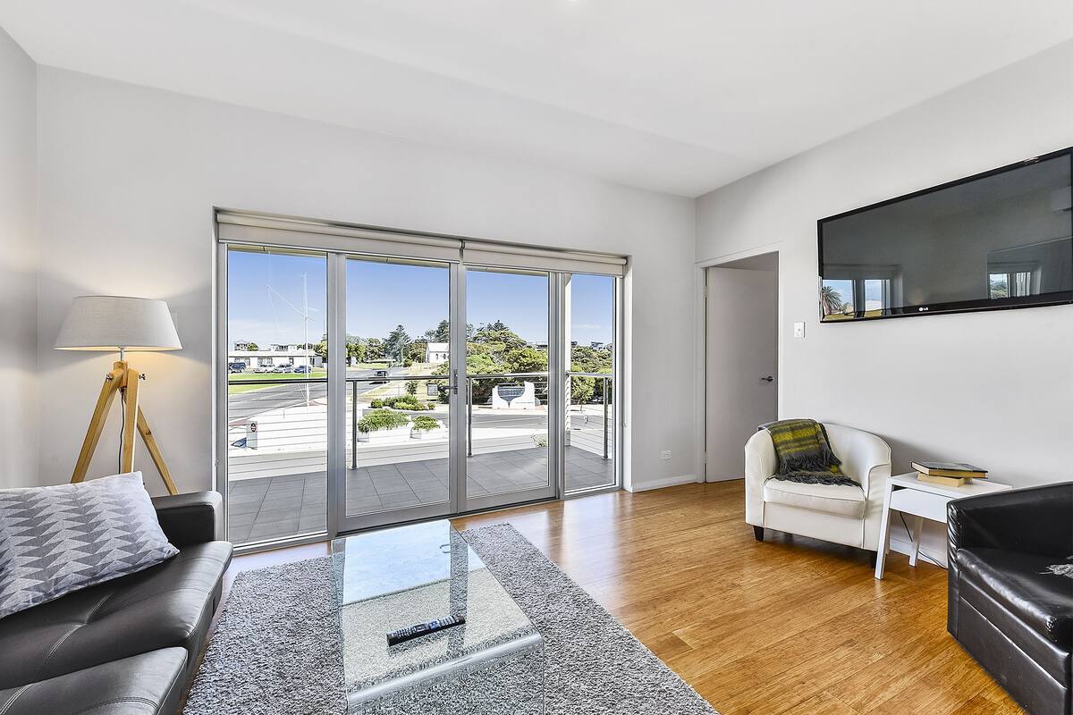 A modern living room with a sofa, a coffee table, a white armchair, and a TV mounted on the wall.