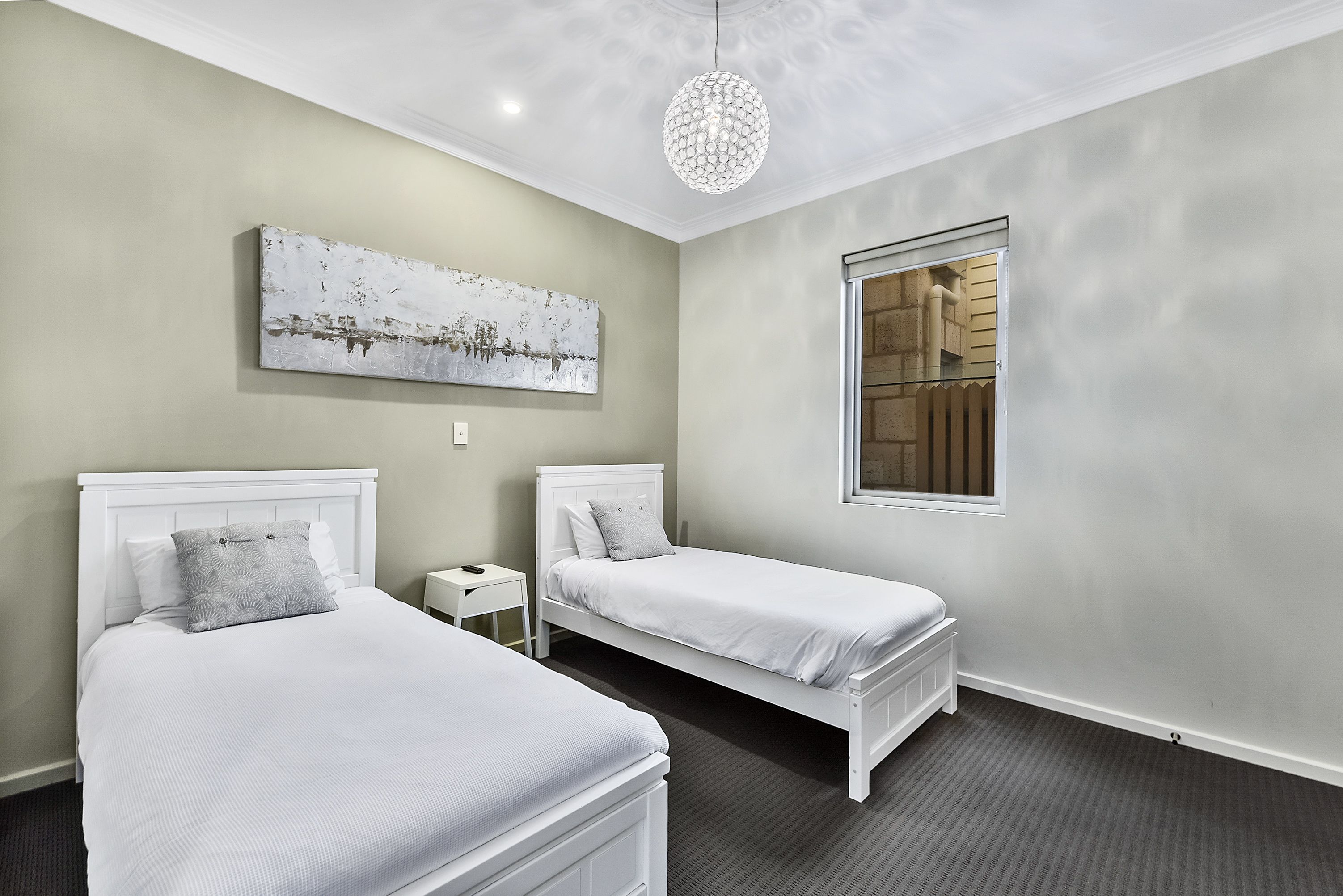Une chambre à coucher avec deux lits blancs, une petite table de chevet, un élément décoratif mural et une grande fenêtre.