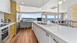 A modern kitchen with a large island, stainless steel appliances, and a view of the sea. - Aloha Waterfront Properties (Robe)