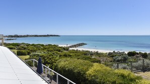 A coastal view from a balcony with a clear sky, a beach, and rocky outcrops in the distance. - Aloha Waterfront Properties (Robe)