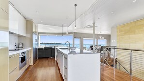 A modern kitchen with a large island, wooden flooring, and a view of the sea. - Aloha Waterfront Properties (Robe)