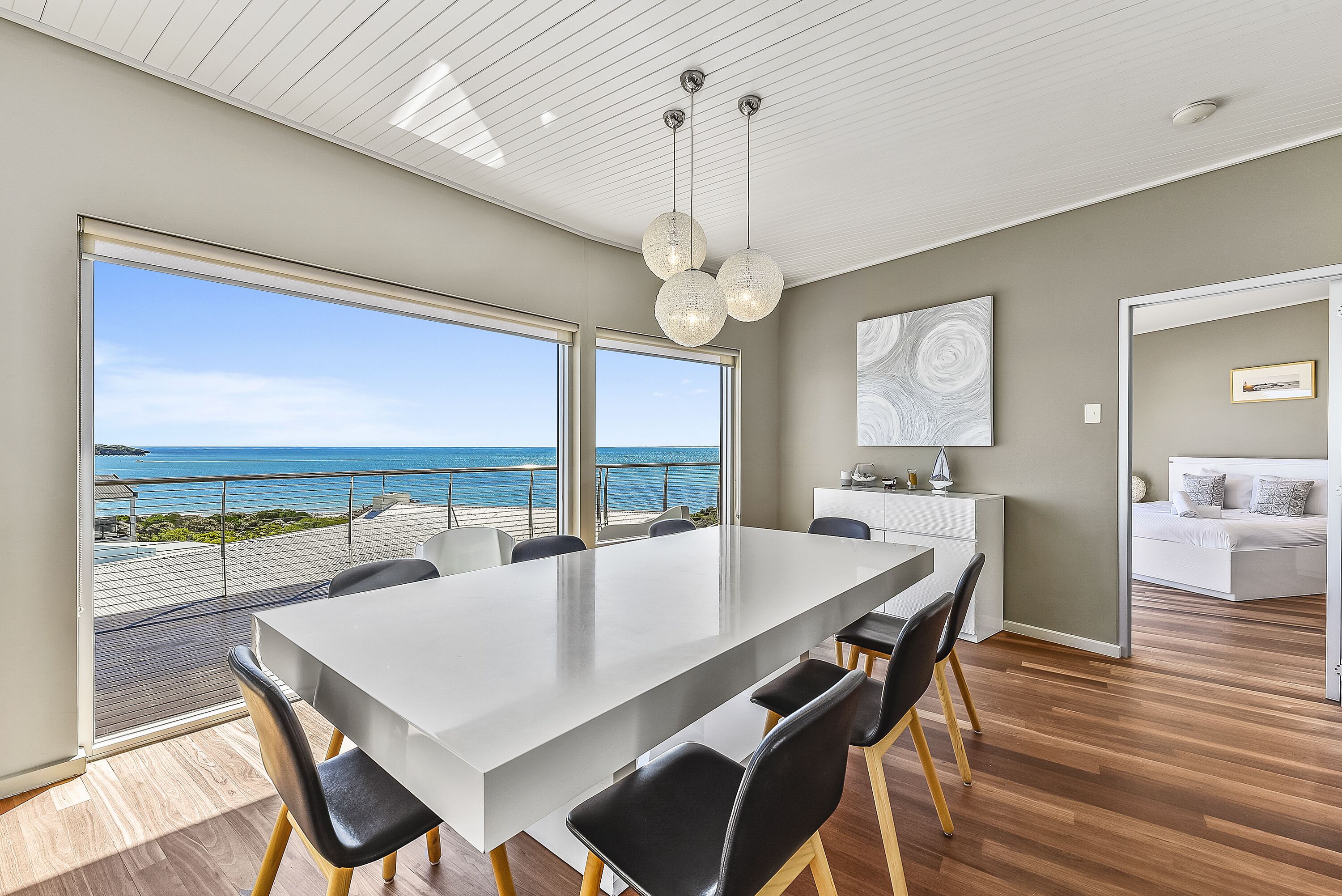 A modern dining area with a large table, chairs, and a view of the ocean.