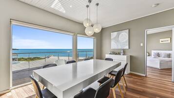 A modern dining area with a large table, chairs, and a view of the ocean.