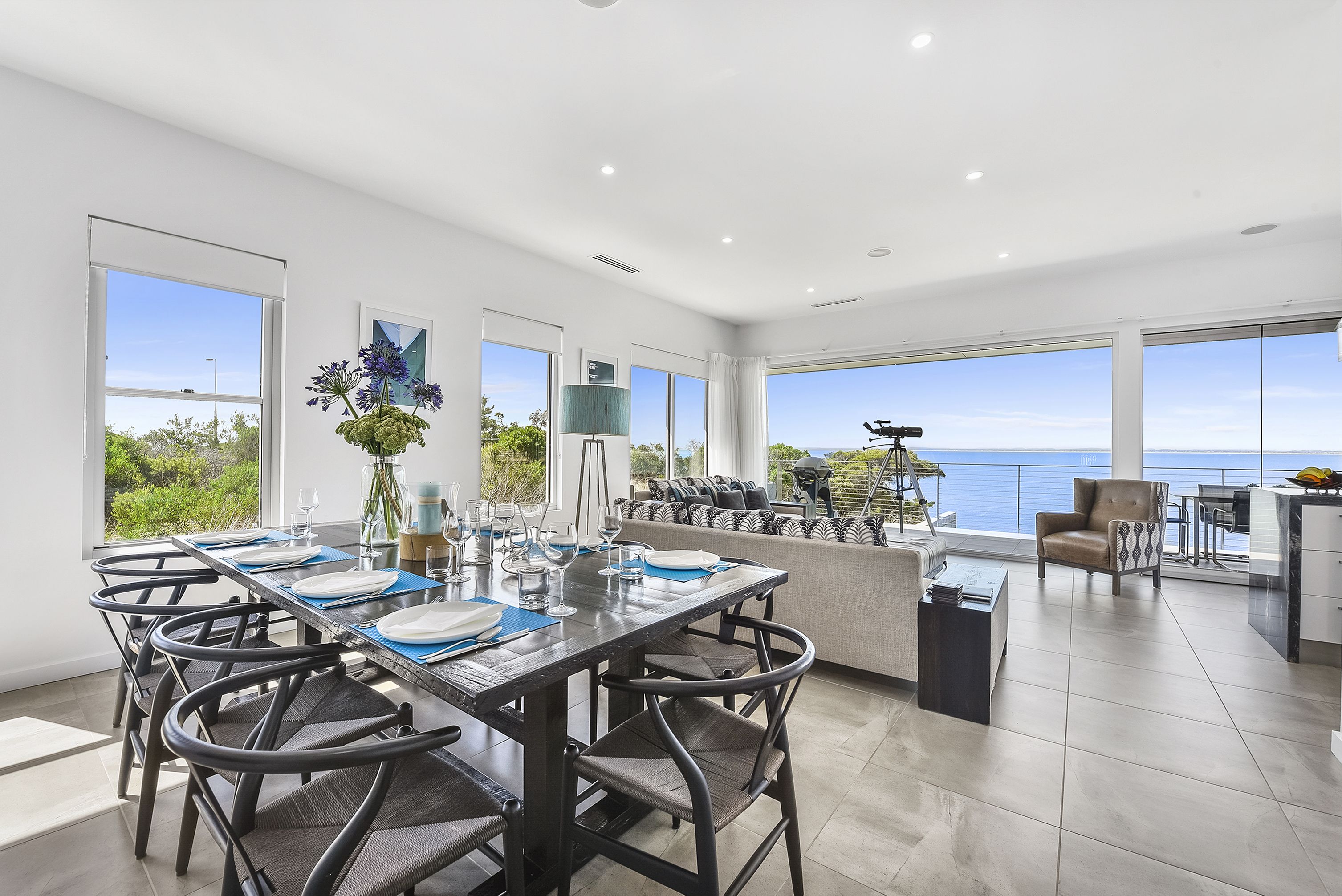 Uma área de refeições moderna com uma mesa longa, cadeiras e vista para o mar.