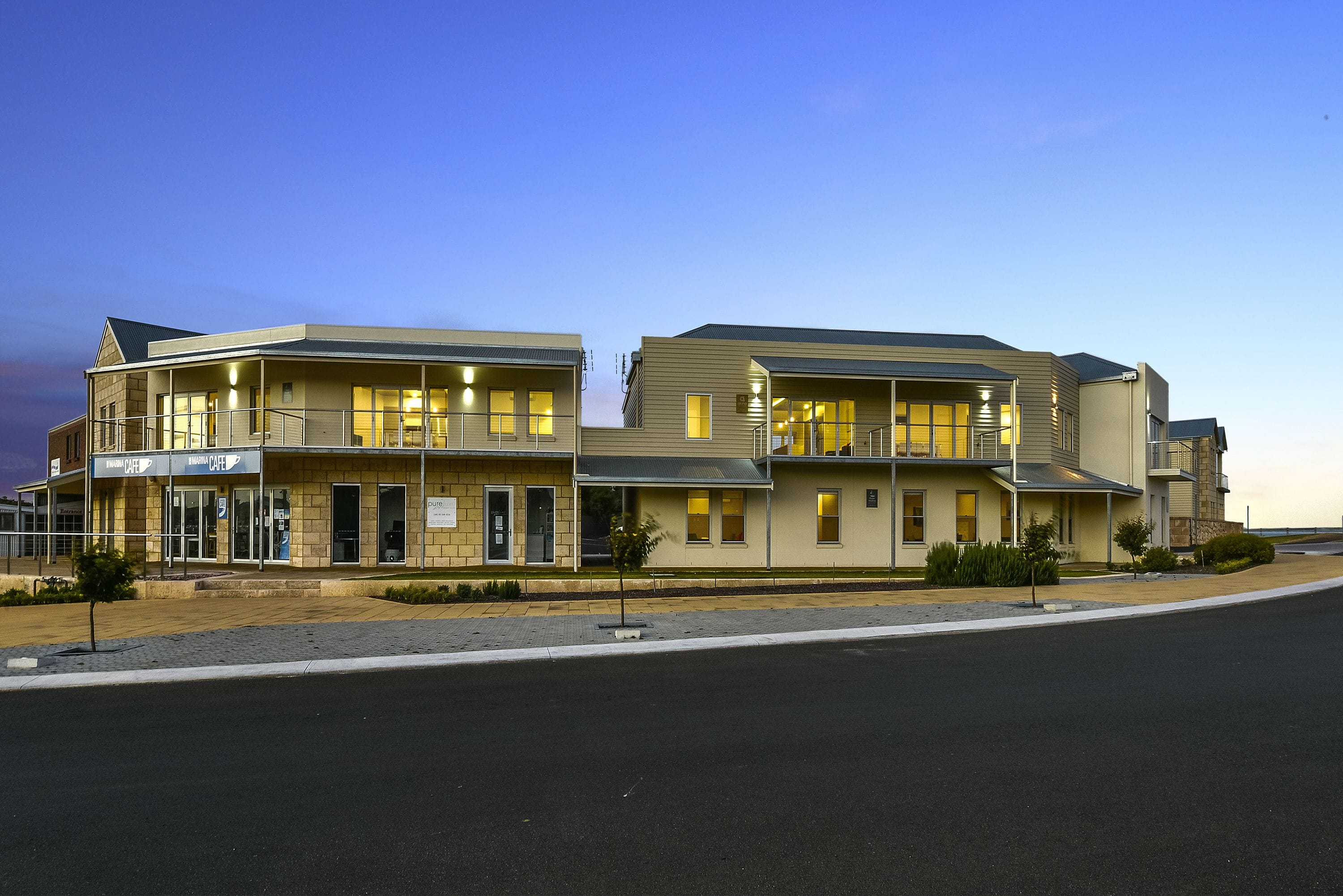 A two-story building with a cafe on the ground floor, a parking lot in front, and a clear sky.